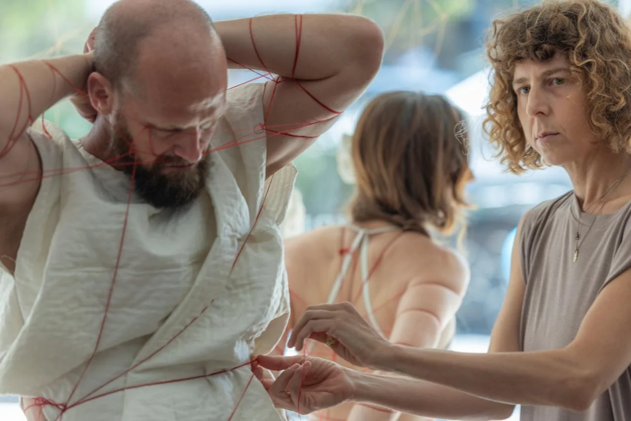 האמנית קושרת את הפרפורמר בחוט אדום, והפרפורמרית ברקע