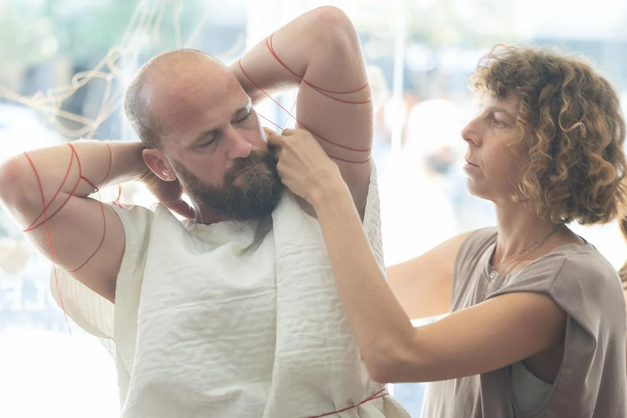האמנית כורכת חוט אדום סביב הפרפורמר, שידיו מאחורי ראשו