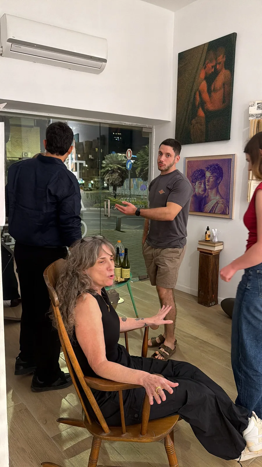 הדוברת מדברת מכיסא העץ ולצידה משתתפים עומדים מול חלון הראווה