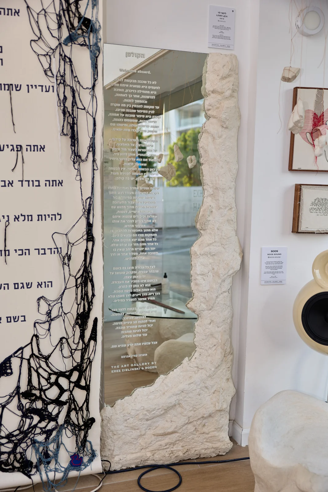 פסל לבן גבוה לצד מראה עם טקסט בפינת הגלריה