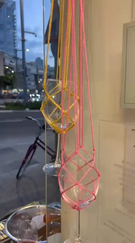 כוסות מקרמה ורודות וצהובות בחלון הראווה בשעת בין ערביים, עם רחוב ואופניים ברקע